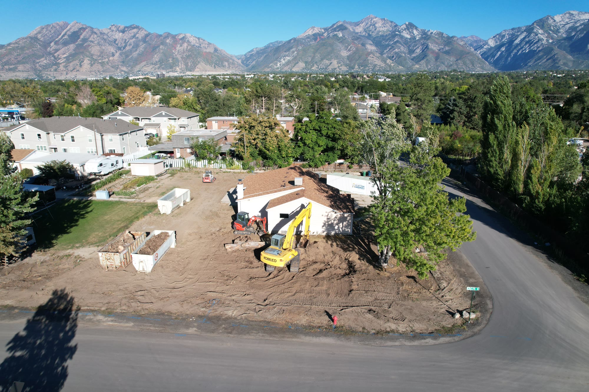 The cleared corner lot with an excavator and the Wasatch behind
