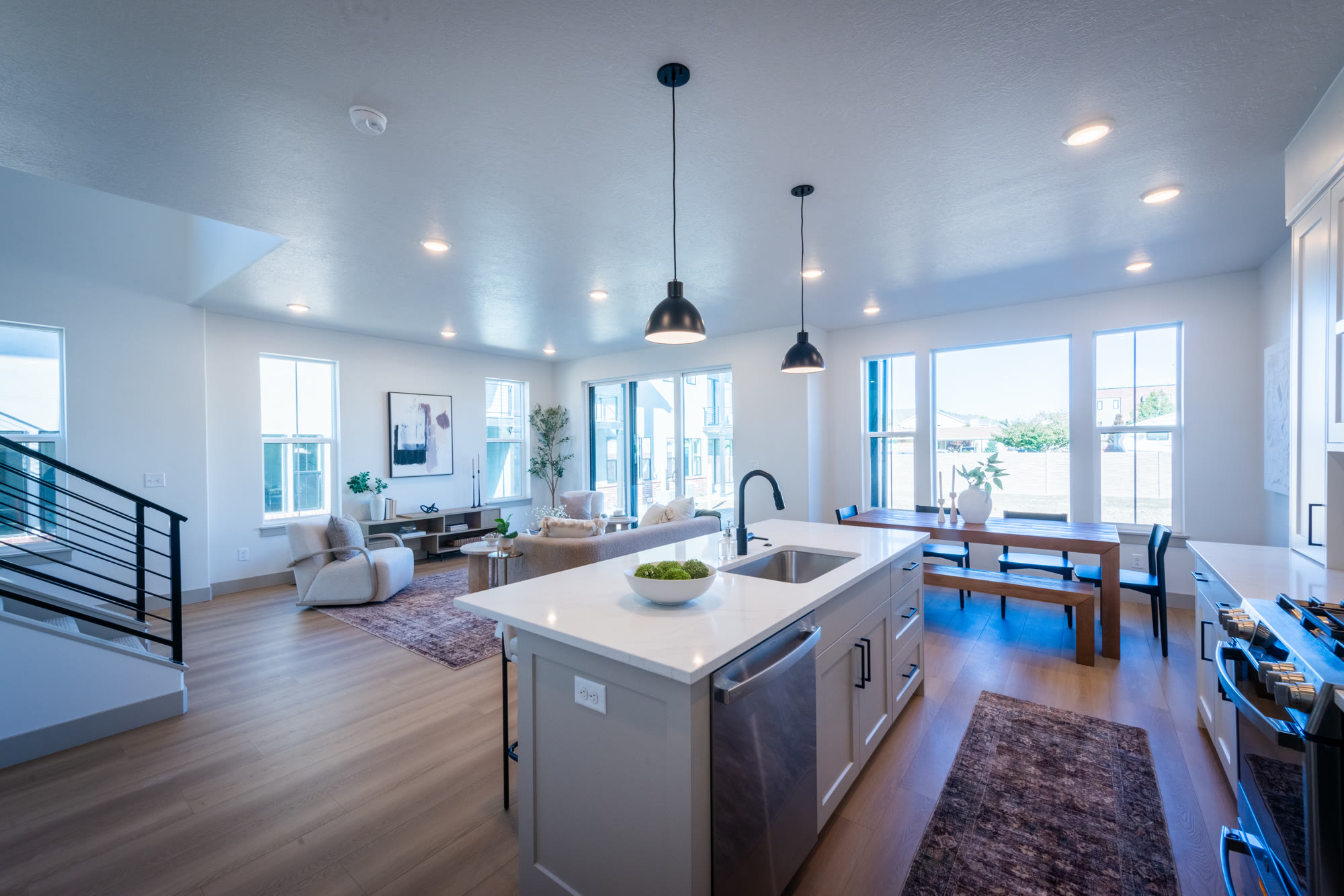 Staged kitchen at Cook's Corner: white island, black pendants, range hood, dining table beyond